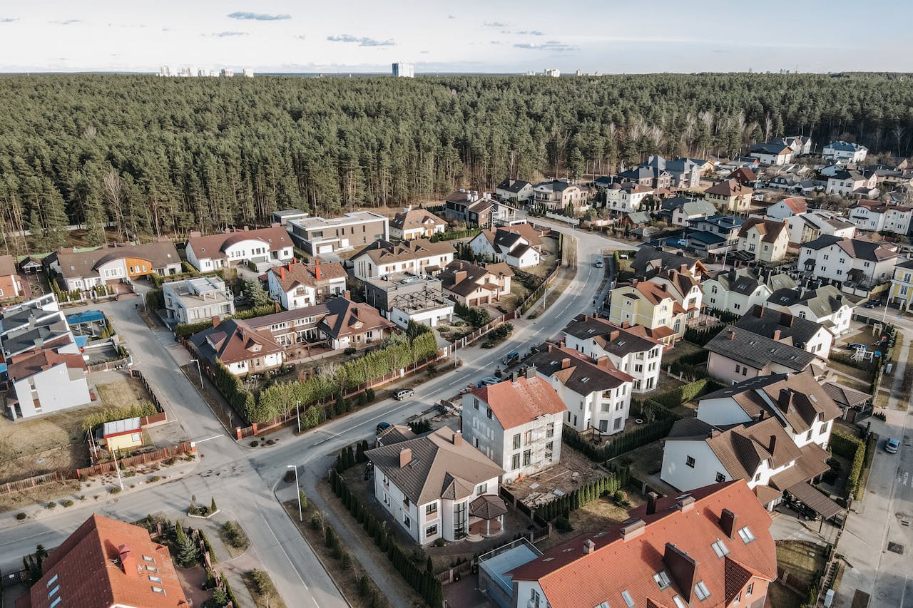 Aerial photo capturing a suburban neighborhood with houses and streets near a forest in spring.